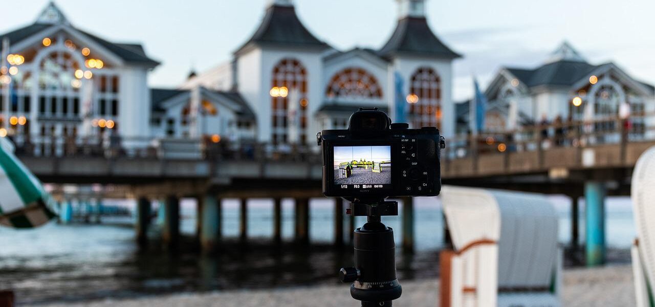 Reisestativ mit Kamera am Strand, im Hintergrund eine Seebrücke.