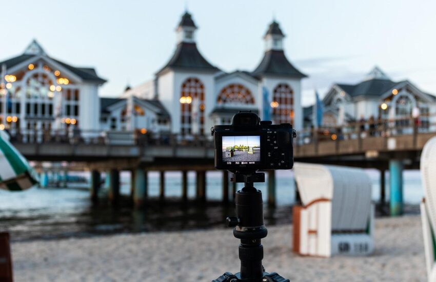 Reisestativ mit Kamera am Strand, im Hintergrund eine Seebrücke.