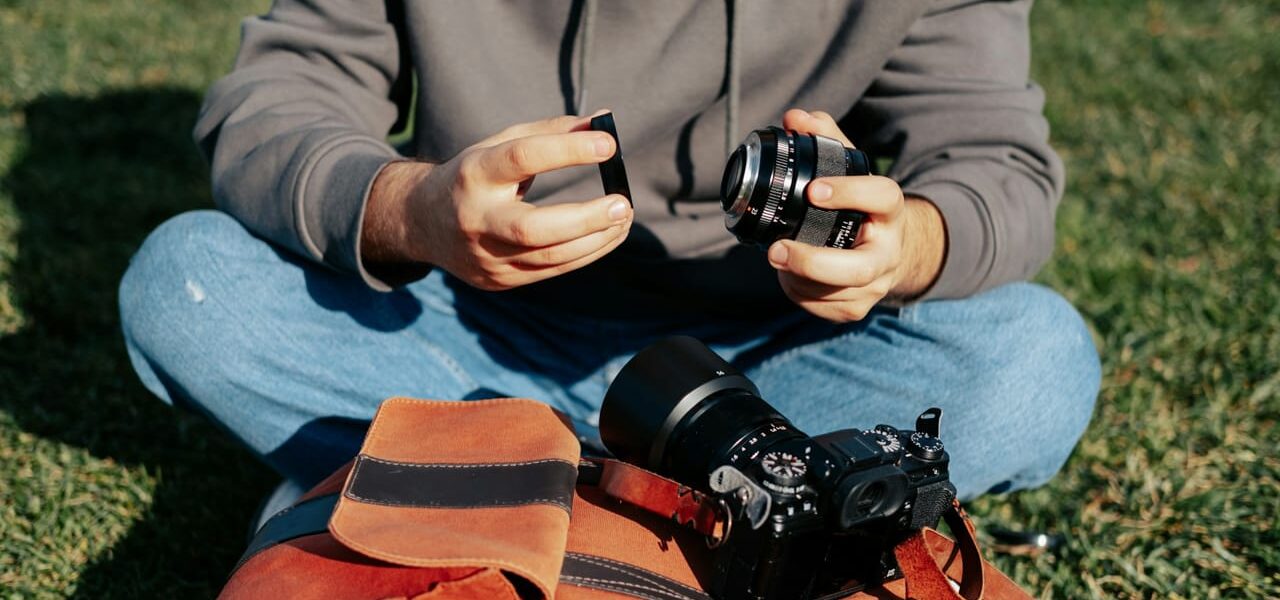 Fotograf sitzt im Freien und wechselt das Objektiv, um Insekten zu fotografieren. Kamera und Ausrüstung liegen auf einer Tasche.