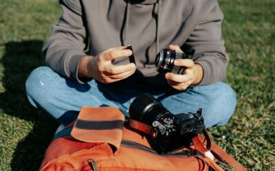 Fotograf sitzt im Freien und wechselt das Objektiv, um Insekten zu fotografieren. Kamera und Ausrüstung liegen auf einer Tasche.