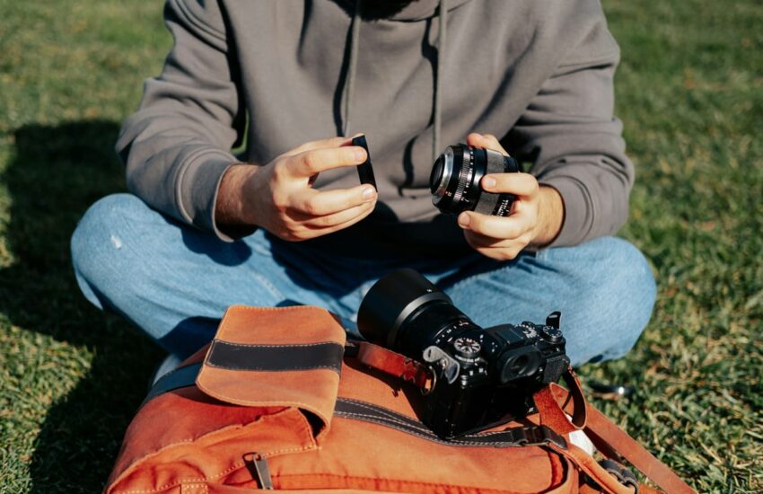 Fotograf sitzt im Freien und wechselt das Objektiv, um Insekten zu fotografieren. Kamera und Ausrüstung liegen auf einer Tasche.