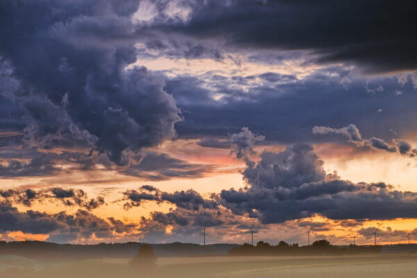 Wolken fotografieren bei Sonnenuntergang – beeindruckende Gewitterstimmung mit Kontrasten Dunkle Gewitterwolken bei Sonnenuntergang über Landschaft mit Windrädern – stimmungsvolles Beispiel zum Wolken fotografieren
