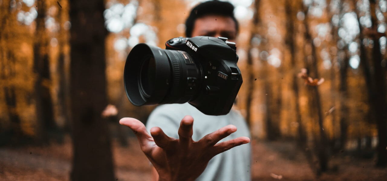 Person wirft eine Kamera in einem herbstlichen Wald in die Luft, symbolisiert kreative Fotografie.