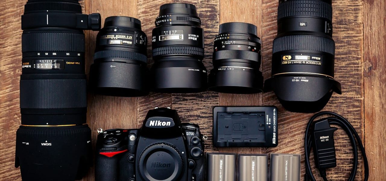 Schwarze Nikon DSLR-Kamera mit mehreren Objektiven und Ladegerät auf einem Holztisch.