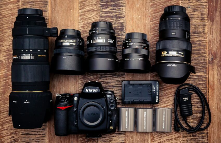 Schwarze Nikon DSLR-Kamera mit mehreren Objektiven und Ladegerät auf einem Holztisch.