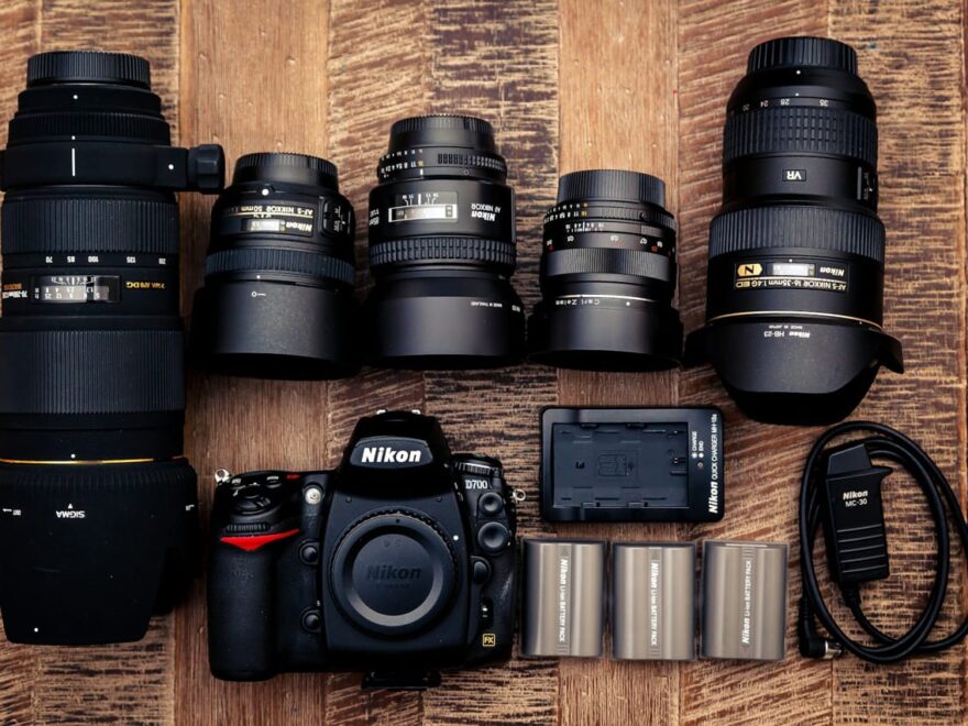 Schwarze Nikon DSLR-Kamera mit mehreren Objektiven und Ladegerät auf einem Holztisch.