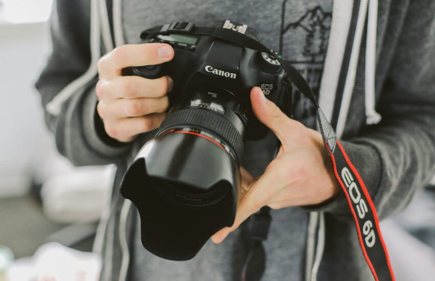 Person hält eine DSLR-Kamera mit Kameragurt, Nahaufnahme der Kamera und des Gurts.