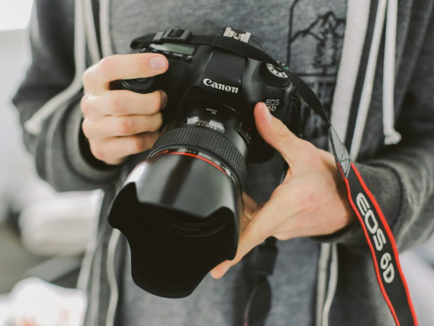 Person hält eine DSLR-Kamera mit Kameragurt, Nahaufnahme der Kamera und des Gurts.