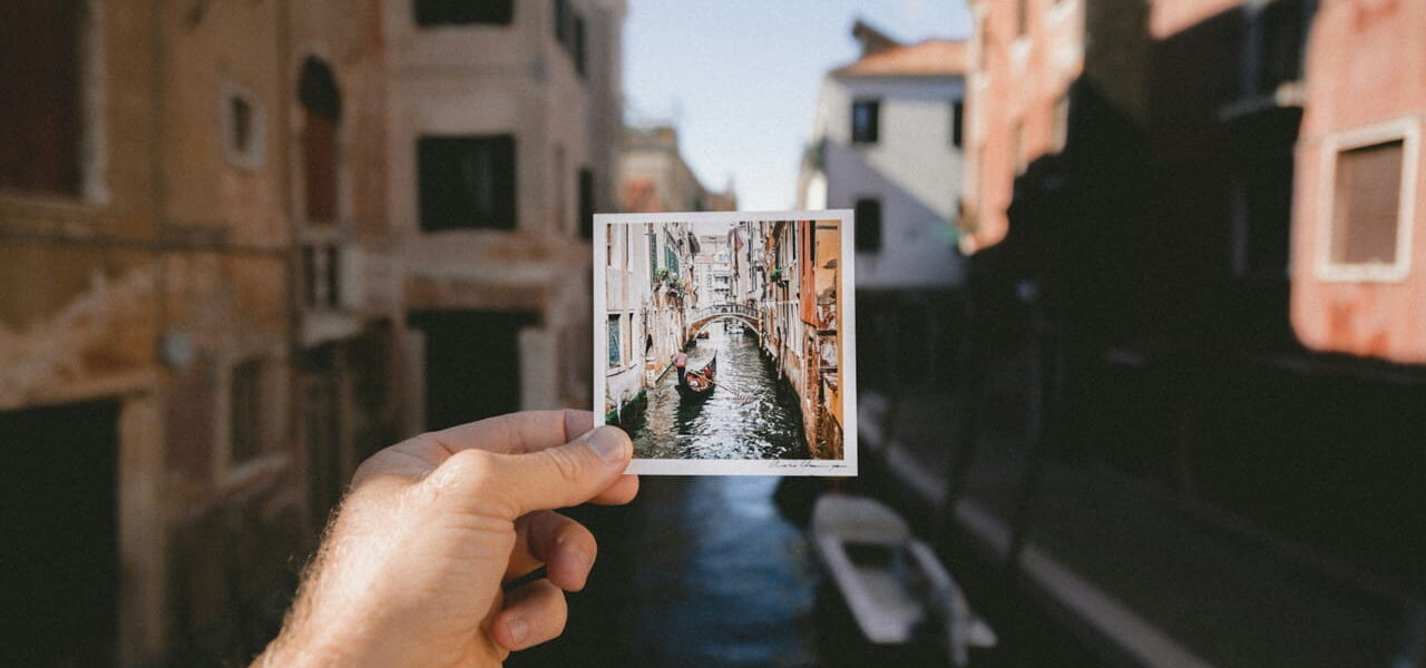 Hand hält ein Reisefotografie-Motiv vor einem Kanal in Venedig