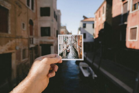 Hand hält ein Reisefotografie-Motiv vor einem Kanal in Venedig