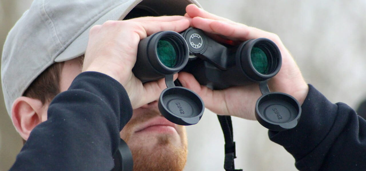 Mann mit Bart nutzt ein Fernglas zur Motivsuche in der Natur