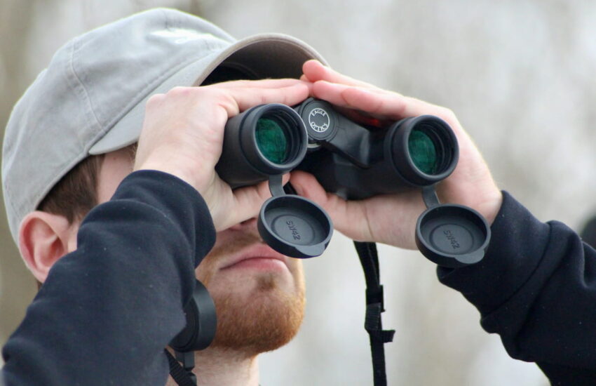 Mann mit Bart nutzt ein Fernglas zur Motivsuche in der Natur
